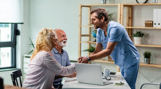 Heureux médecin saluant un couple de personnes âgées et serrant la main d'une femme à son bureau