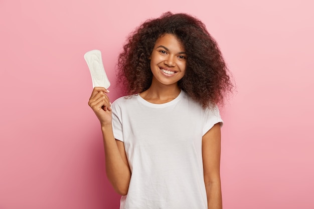 Heureux modèle féminin bouclé attrayant tient une serviette hygiénique mince