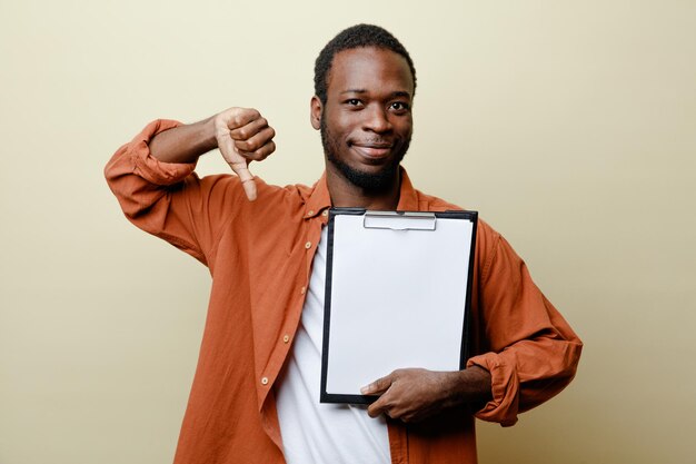 Heureux montrant les pouces vers le bas jeune homme afro-américain tenant le presse-papiers isolé sur fond blanc