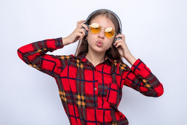 Heureux de montrer le geste de baiser belle petite fille portant une chemise rouge et des lunettes avec un casque