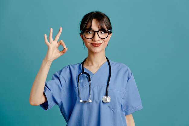 Heureux de montrer un geste correct jeune femme médecin portant un stéthoscope fith uniforme isolé sur fond bleu