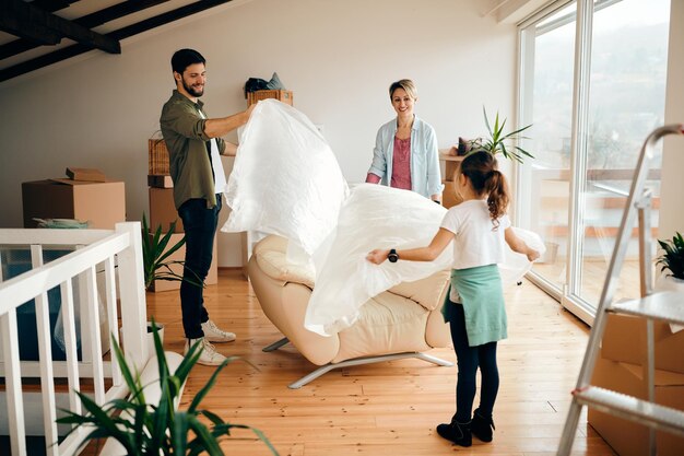 Heureux parents avec fille déballant des meubles lors d'un déménagement dans une nouvelle maison