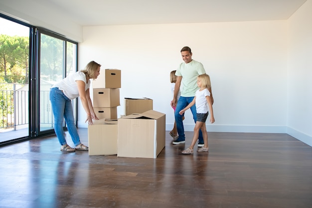 Heureux parents et filles ouvrant des boîtes et déballant des choses dans leur nouvel appartement vide