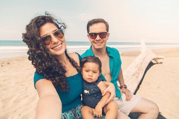 Heureux parents souriant et prenant selfie sur la plage.