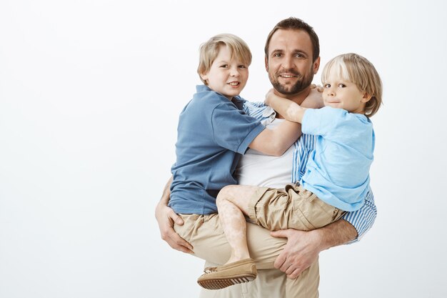 Heureux père européen tenant deux garçons sur les mains et souriant largement, étant heureux et aimant ses fils, famille unie et proche