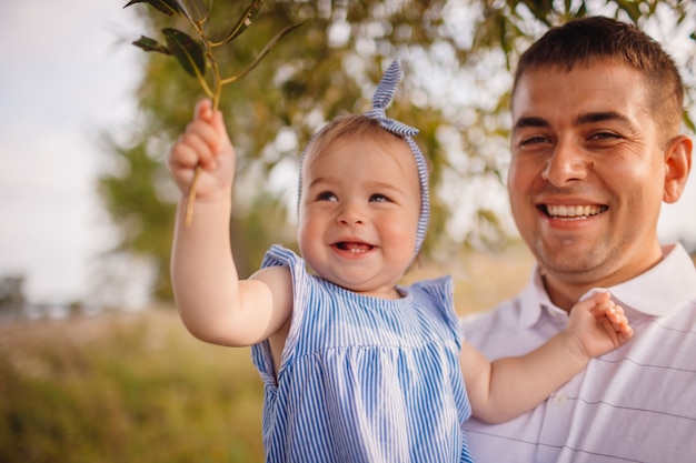 Photo gratuite heureux père tient une charmante petite fille debout dans le jardin