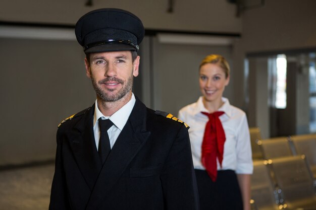 Heureux pilote et hôtesse de l'air debout dans le terminal de l'aéroport