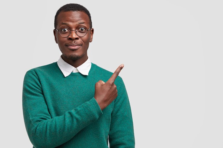Photo gratuit heureux les points adultes masculins hipster avec l'index dans le coin supérieur droit, vêtus de vêtements élégants