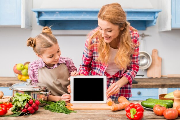 Heureux portrait de mère et fille regardant une tablette numérique sur un bureau en bois