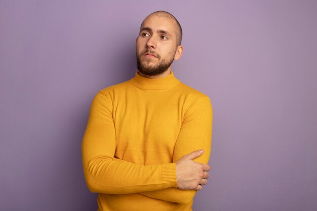 Heureux regardant côté jeune beau mec croisant les mains isolés sur violet avec copie espace