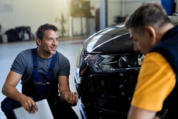 Heureux réparateur automobile et son collègue communiquant tout en travaillant ensemble dans un atelier