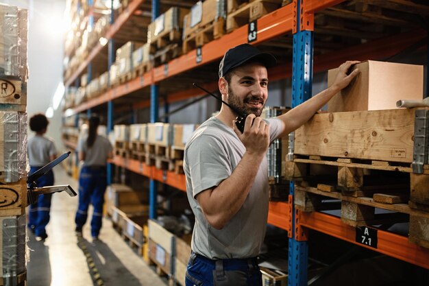 Heureux répartiteur utilisant un talkie-walkie tout en travaillant dans un entrepôt de distribution