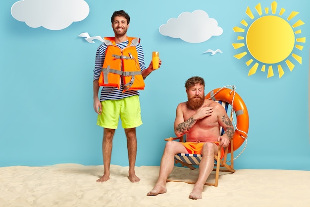 Heureux sauveteur et mec brûlé par le soleil posant à la plage