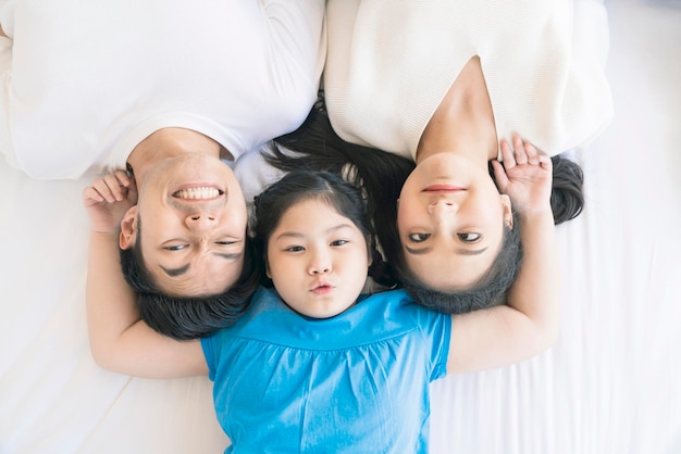 Heureux séduisant jeune asiatique Portrait de famille harmonie saine dans la vie concept de journée familiale homme de famille asiatique femme et petite fille s'amusant ensemble vue de dessus matelas de chambre
