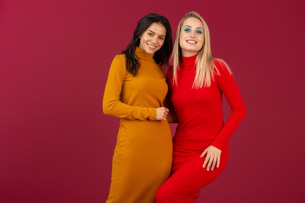 Heureux souriant femmes assez élégantes en robe tricotée jaune et rouge automne hiver mode posant isolé sur mur rouge