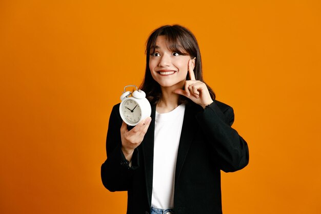 Heureux tenant réveil jeune belle femme portant une veste noire isolée sur fond orange