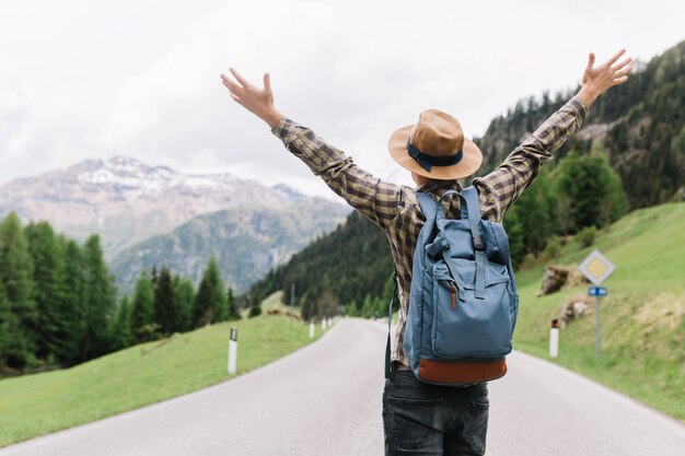 Heureux voyageur masculin posant avec les mains debout sur l'autoroute et regardant les arbres lointains