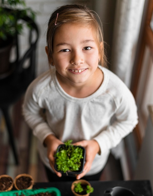High angle of smiley little girl holding plant en pot à la maison