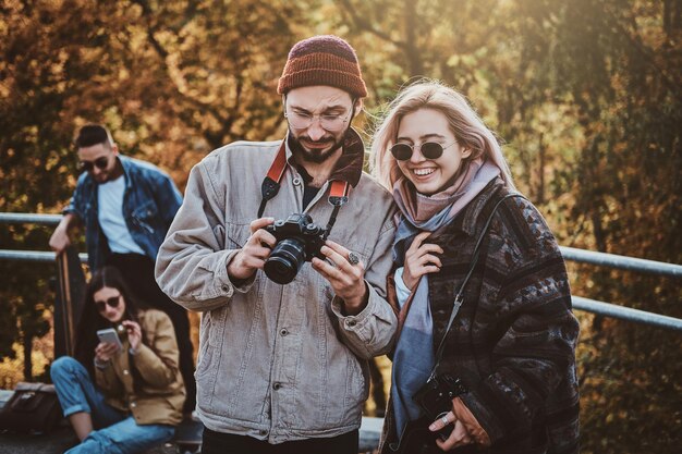 Hipster attrayant montre des photos pour sa petite amie souriante au parc d'automne.