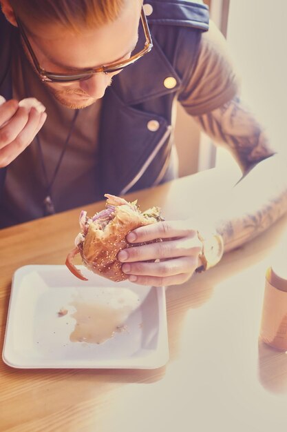 Hipster attrayant vêtu d'une veste en cuir mangeant un hamburger végétalien.