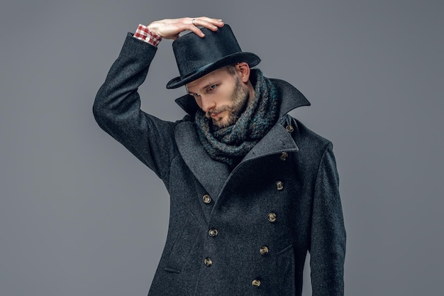 Un hipster barbu vêtu d'une veste grise et d'un chapeau cylindrique isolé sur fond gris.
