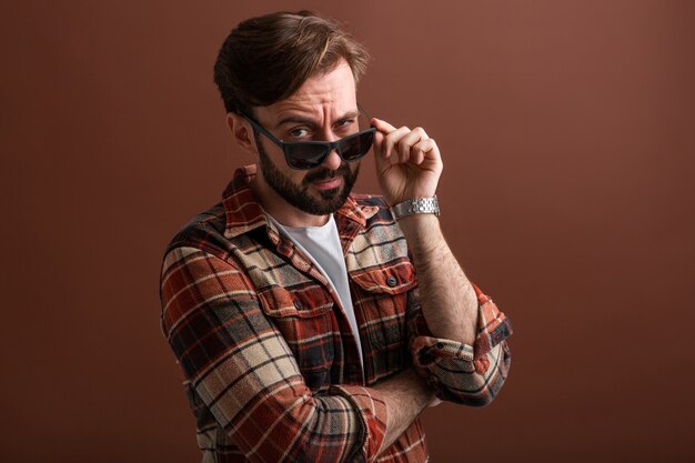 Hipster émotionnel bel homme barbu élégant avec une expression de visage drôle sur brun