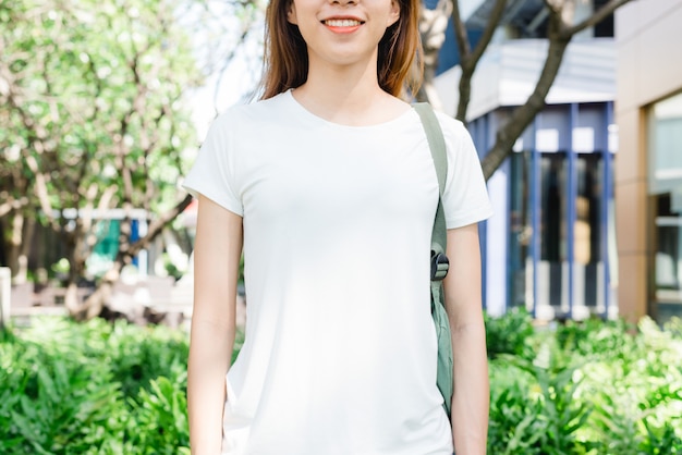 Hipster fille asiatique longs cheveux bruns en t-shirt blanc vierge est debout au milieu de la rue. Un fem