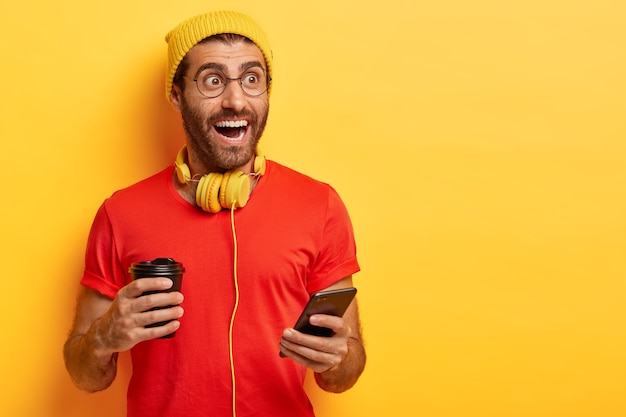 Hipster heureux en tenue décontractée tient une tasse de café et un téléphone portable