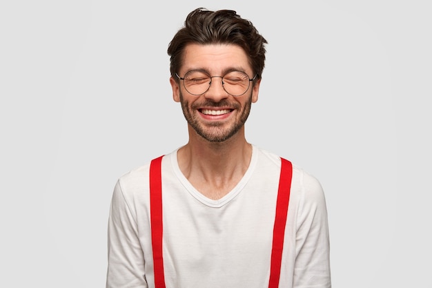 Hipster homme gai à la mode avec un sourire à pleines dents, ferme les yeux du rire