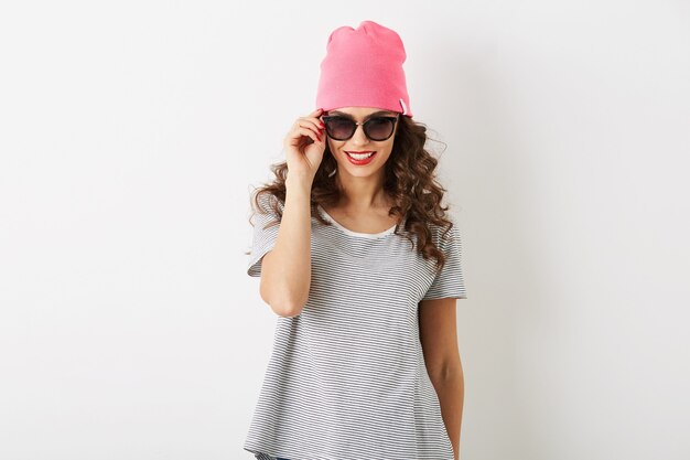 Hipster jolie femme au chapeau rose, lunettes de soleil, souriant, isolé, dents blanches, lèvres rouges, cheveux bouclés, portant un t-shirt