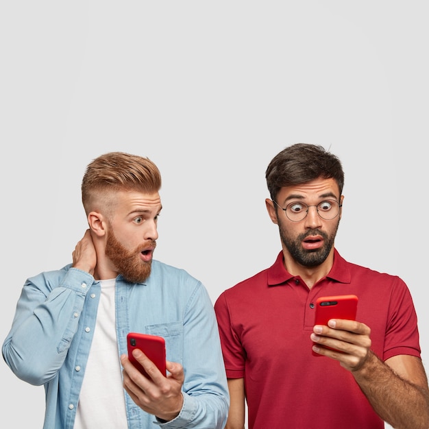 Photo gratuite hipsters masculins surpris à la recherche de smartphones