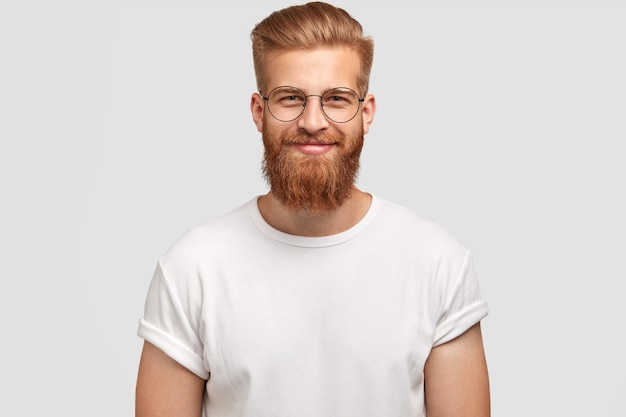 Photo gratuite hispster à la mode joyeux ravi avec barbe au gingembre, porte des lunettes rondes et un t-shirt blanc