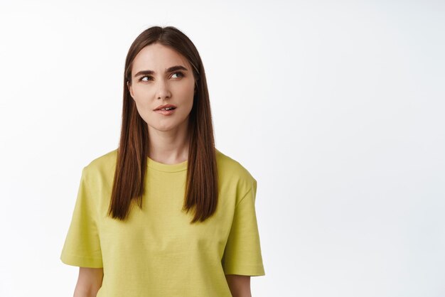 Hmm intéressant Une femme réfléchie se mord la lèvre et regarde de côté le nuage de pensée ayant l'idée de réfléchir à qch debout en t-shirt sur fond blanc