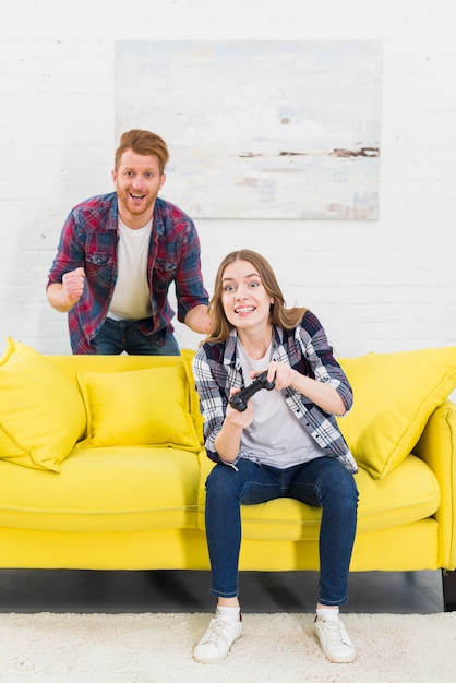 Homme acclamant sa copine jouant à la console de jeu avec des manettes de jeu à la maison