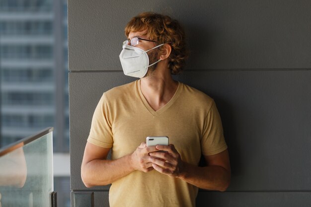 Homme adulte barbu blanc à l'aide de smartphone tout en portant un masque chirurgical sur un mur industriel. Santé, épidémies, réseaux sociaux.