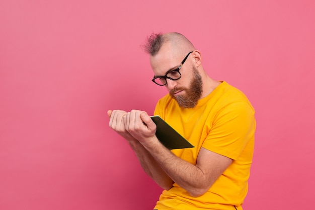 Homme adulte barbu européen dans des verres lire livre isolé sur rose