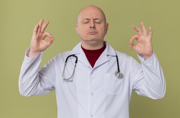 Homme adulte confiant en uniforme de médecin avec stéthoscope méditant debout les yeux fermés