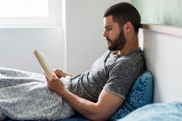 Photo gratuite homme adulte couché dans son lit et lisant