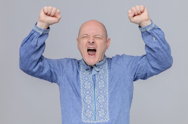 Homme adulte excité en chemise bleue debout avec les poings levés