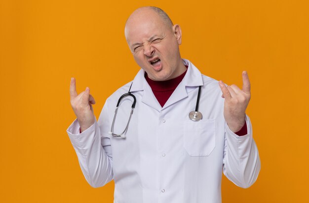 Homme adulte excité en uniforme de médecin avec signe de cornes gesticulant stéthoscope