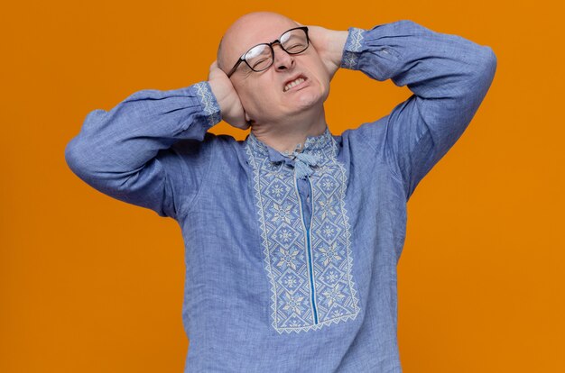 Homme adulte mécontent en chemise bleue et avec des lunettes fermant ses oreilles avec les mains