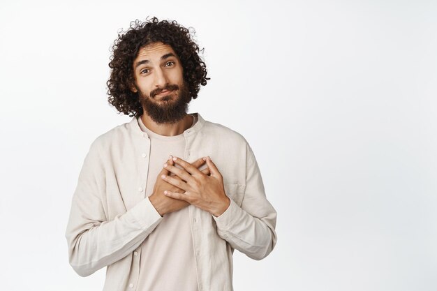 Homme adulte mignon et attentionné, tenant la main sur le cœur, l'air touché et flatté, reconnaissant pour quelque chose debout sur fond blanc