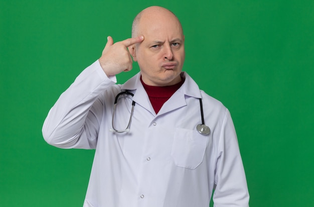 Homme adulte réfléchi en uniforme de médecin avec stéthoscope mettant le doigt sur sa tempe et regardant