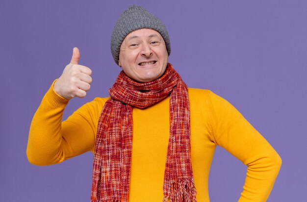 Homme adulte souriant avec un chapeau d'hiver et une écharpe autour du cou, levant le pouce