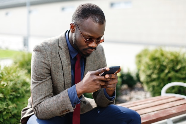 Photo gratuite homme d'affaires africain-américain travaille dans son smartphone assis sur le banc à l'extérieur