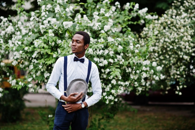 Photo gratuite homme d'affaires afro-américain élégant au pantalon avec jarretelles et chemise avec chapeau noeud papillon posé en plein air