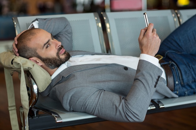 Homme d'affaires à l'aide de téléphone portable en position couchée sur des chaises dans la zone d'attente