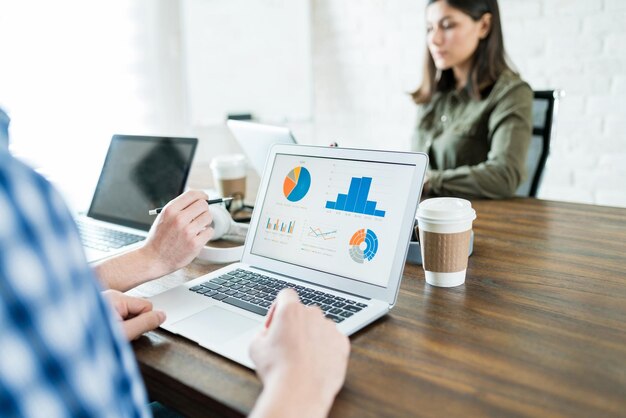 Homme d'affaires analysant des graphiques sur un ordinateur portable tout en travaillant avec un collègue au bureau