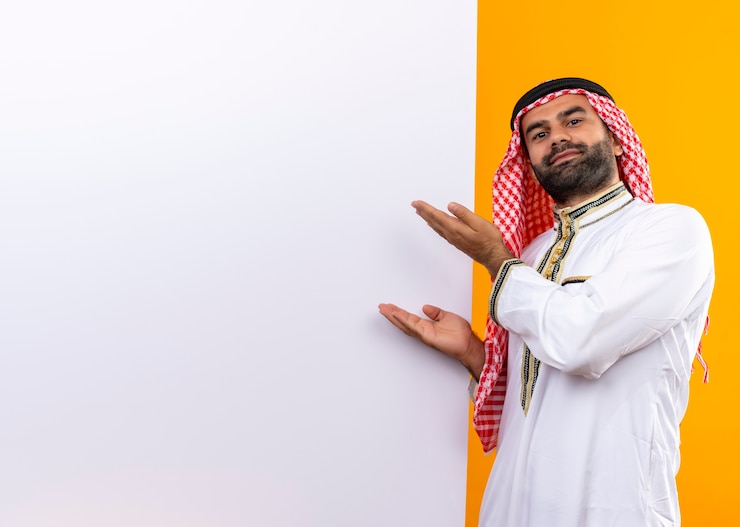 Photo gratuit homme d'affaires arabe en vêtements traditionnels présentant des bras d'affichage vierge debout sur un mur orange