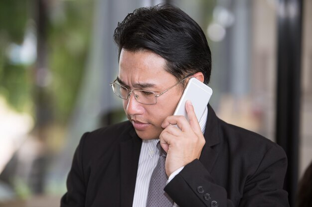 Homme d'affaires asiatique portant des lunettes en costume parlant sur téléphone mobile